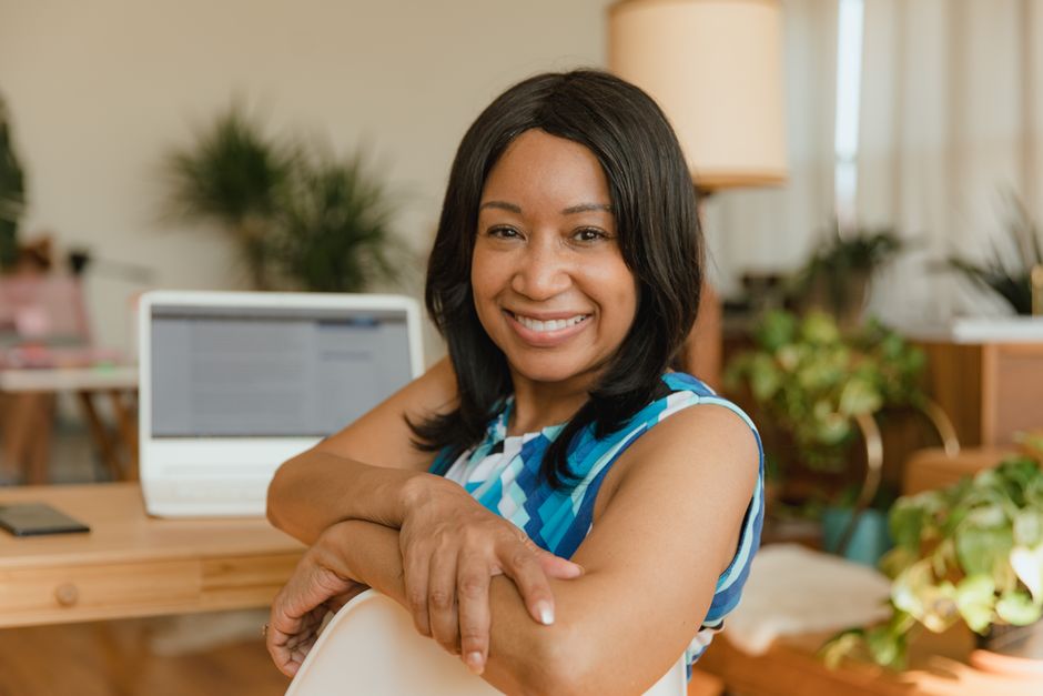 A woman smiling at her desk beside a laptop in a bright office.